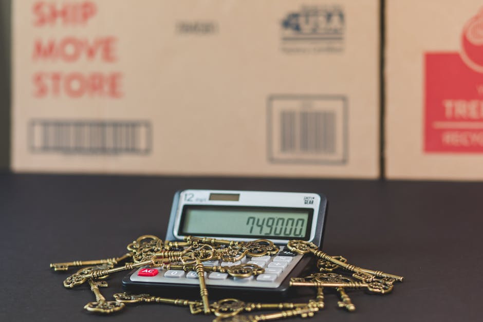 A close-up view of a hand holding a pink miniature house model, positioned among small black house models on a cluttered surface. The scene includes a rolled-up 200 euro banknote, a calculator, and va